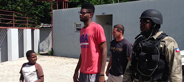 A little Haitian onlooker walks beside Nerlens Noel as he prepares to enter Gymnasium Vincent with manager Chris Driscoll and Port-au-Prince police officer Ricot "Mutombo" St. Louis. (Keith Pompey/Staff) - Click Picture for Source 
